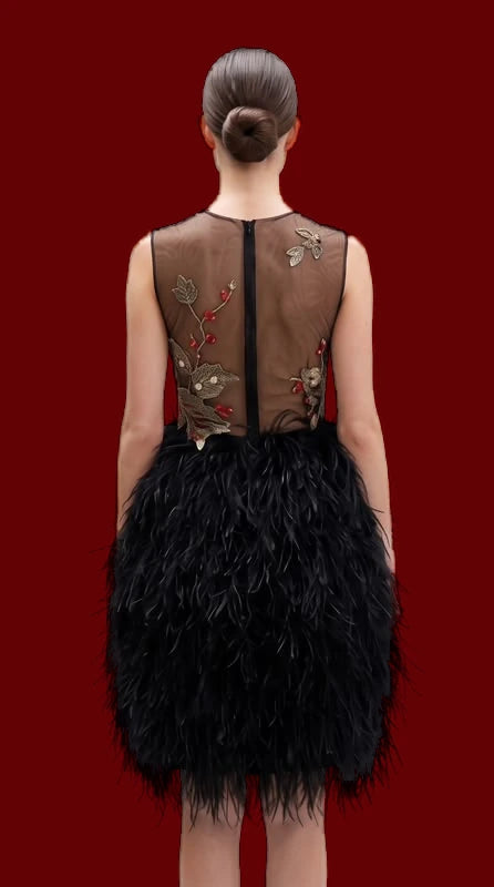 A short black dress with a feathered skirt and a sheer bodice embroidered in gold.