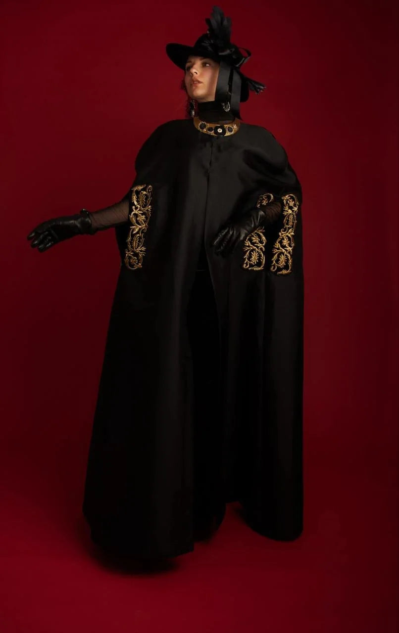 A black cape abaya with gold couched embroidery at the sleeves, photographed against red.