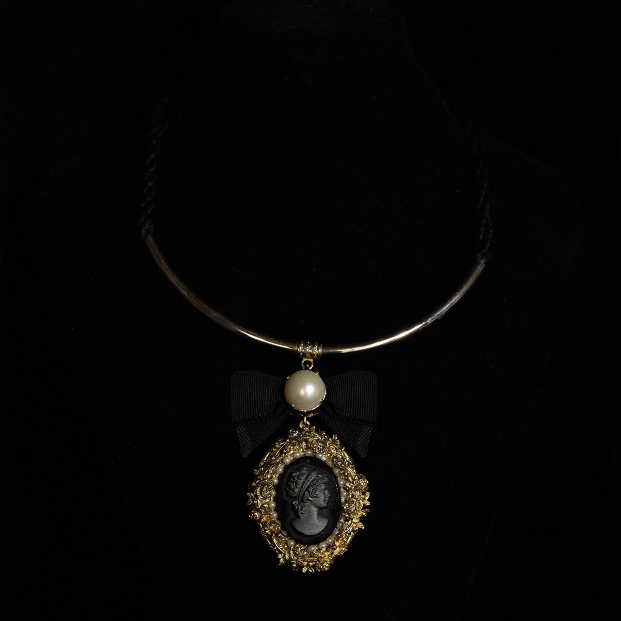 Rigid gold-tone collar necklace with a black cameo pendant in a filigree frame