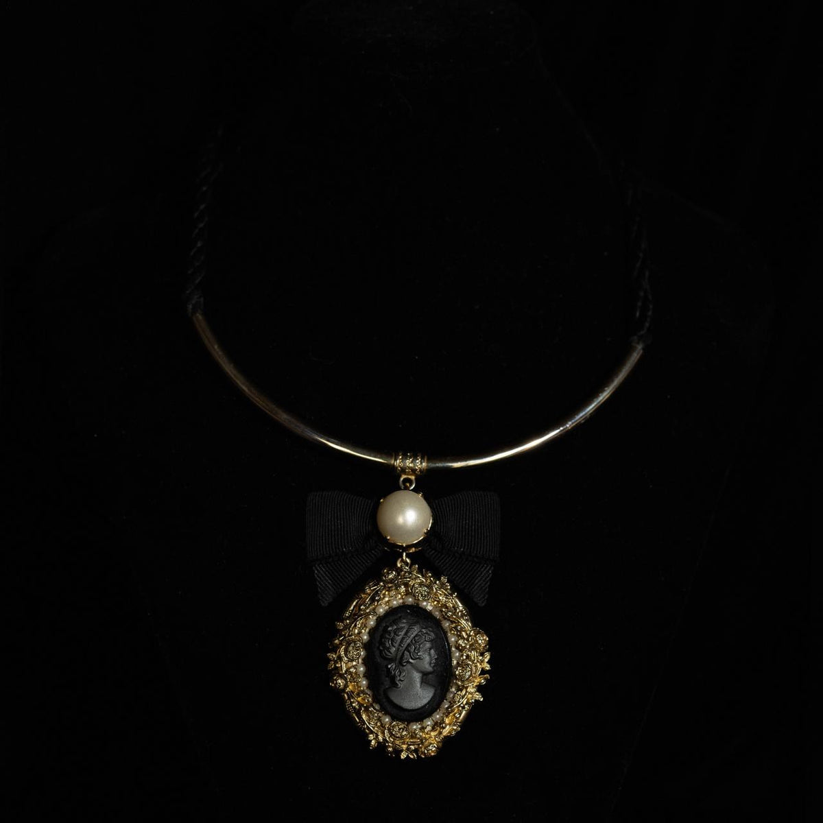 Rigid gold-tone collar necklace with a black cameo pendant in a filigree frame