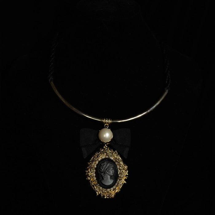 Rigid gold-tone collar necklace with a black cameo pendant in a filigree frame