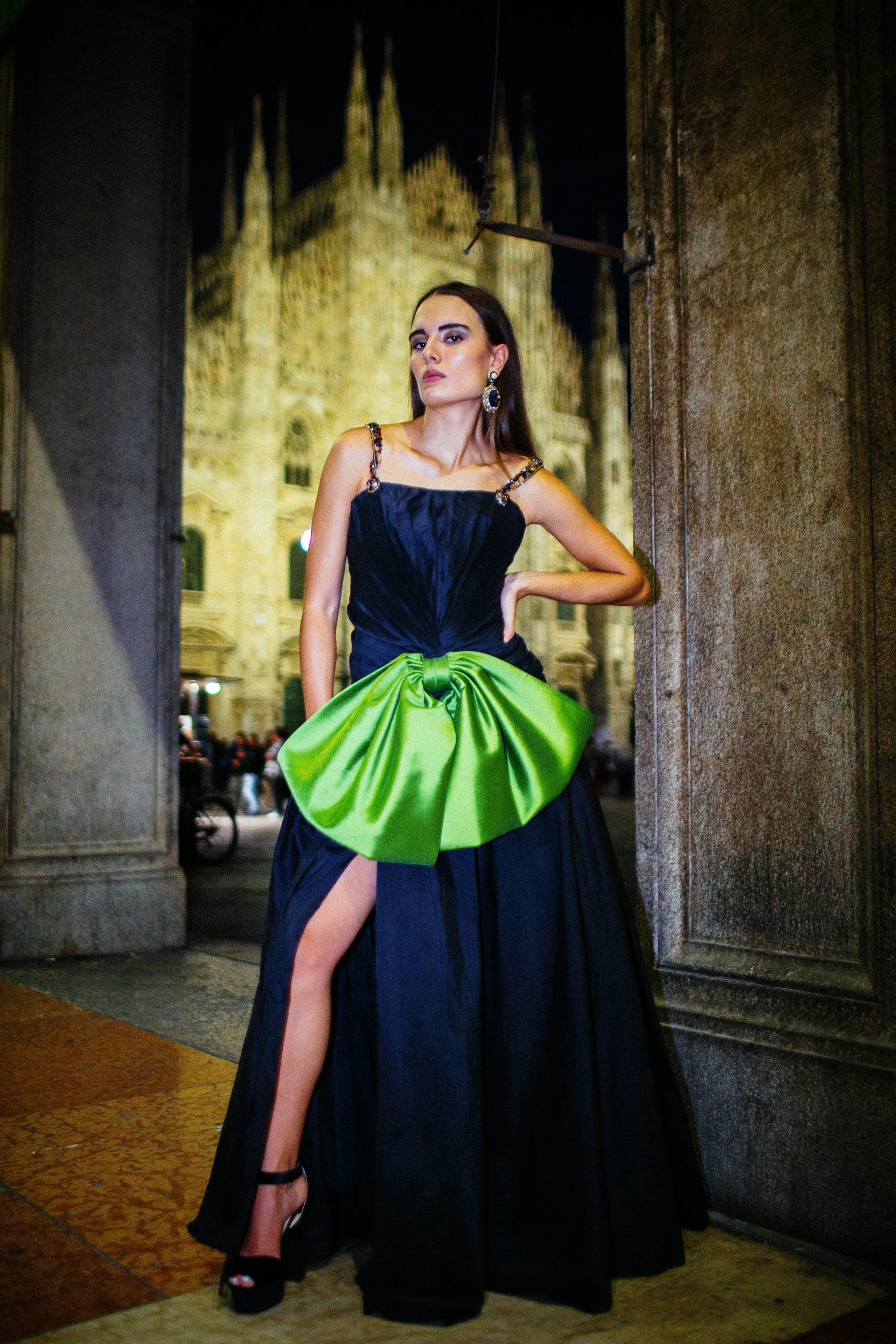 A navy gown with a large green satin bow gathered at the hip, photographed in Milan at night.