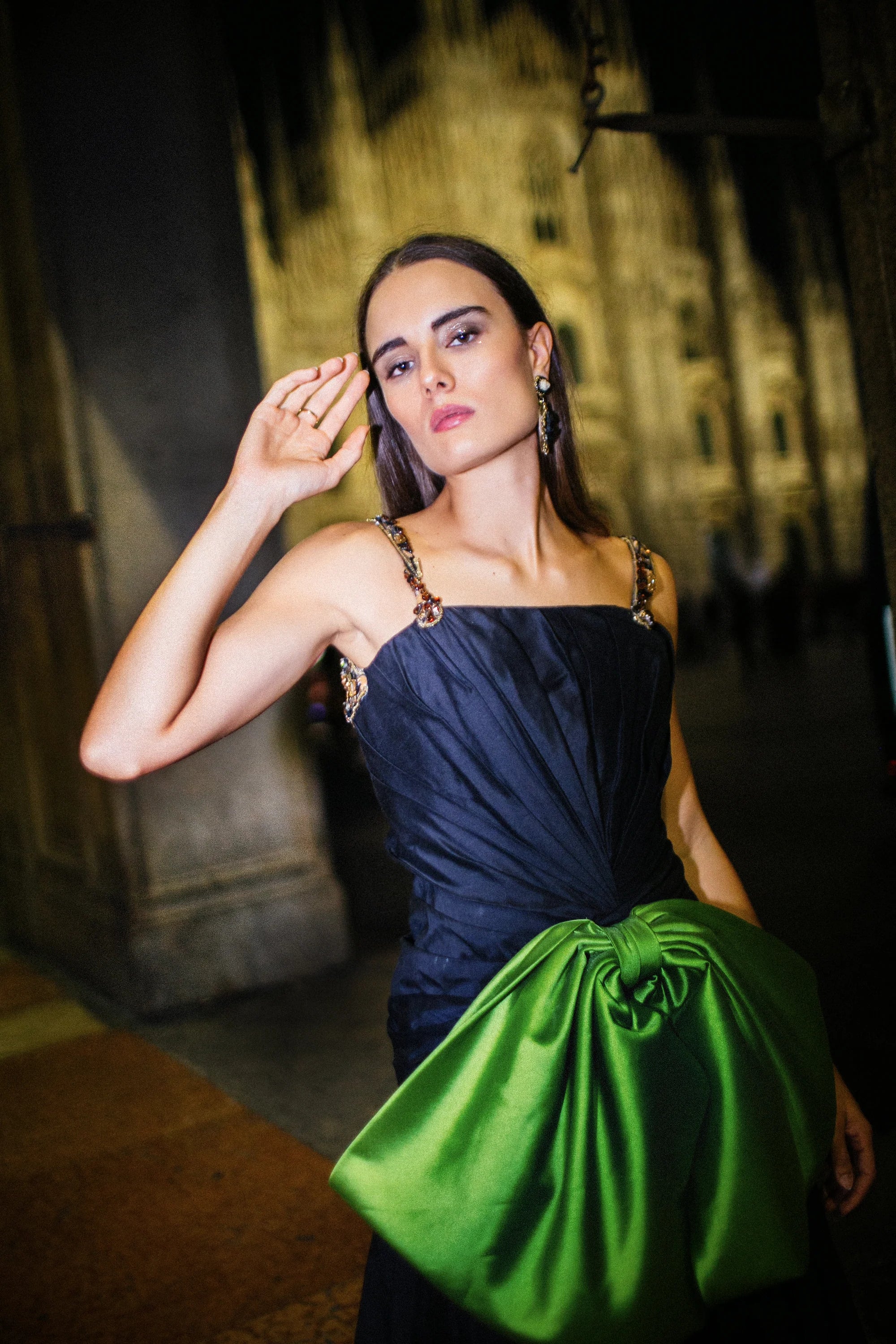 A navy gown with a large green satin bow gathered at the hip, photographed in Milan at night.