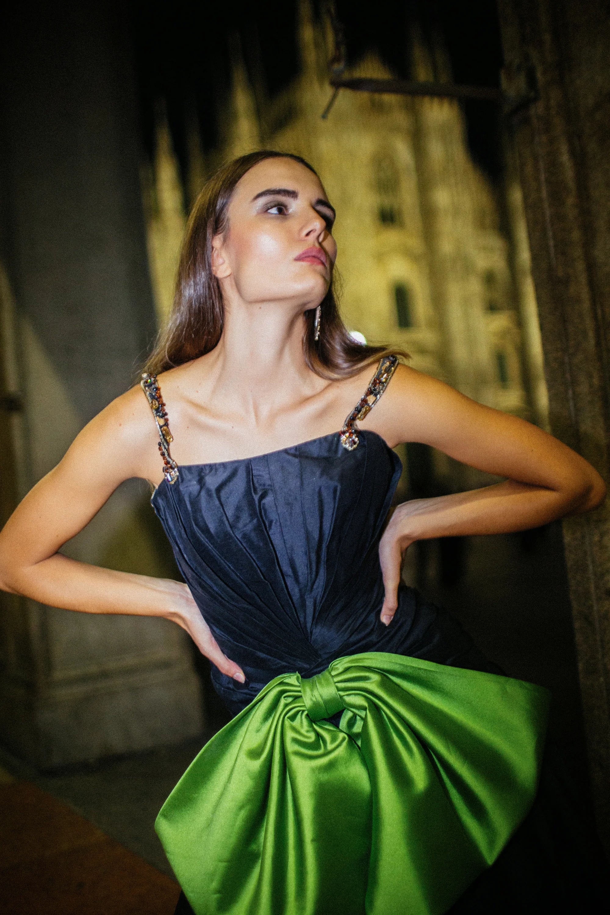 A navy gown with a large green satin bow gathered at the hip, photographed in Milan at night.