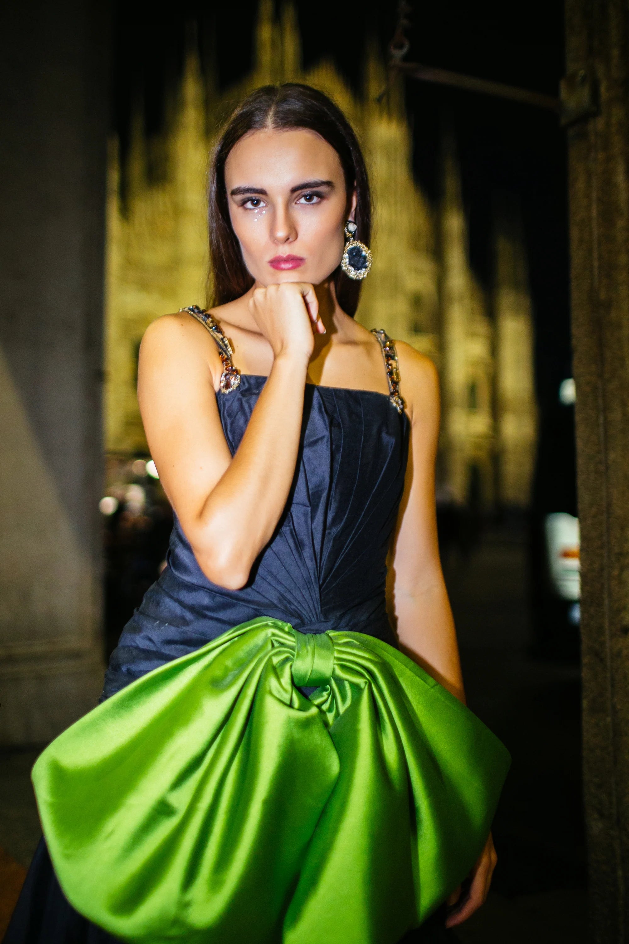 A navy gown with a large green satin bow gathered at the hip, photographed in Milan at night.
