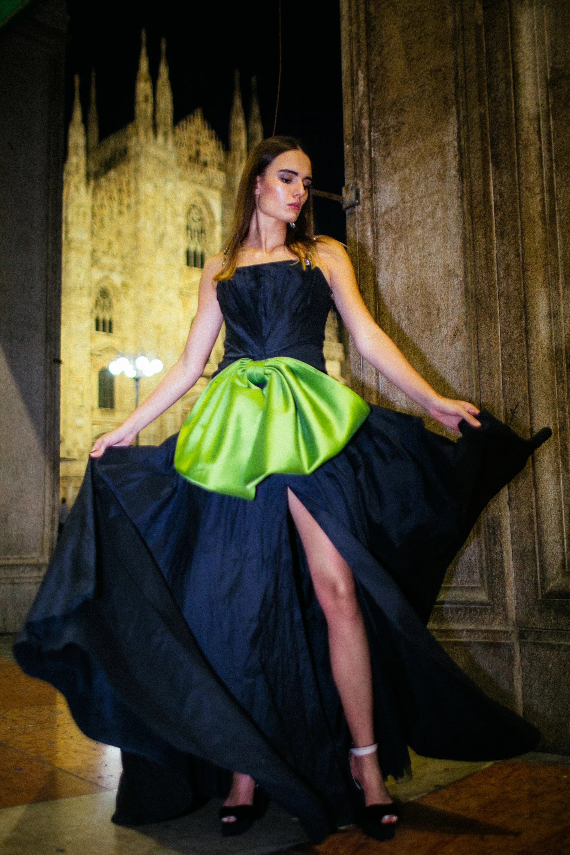A navy gown with a large green satin bow gathered at the hip, photographed in Milan at night.