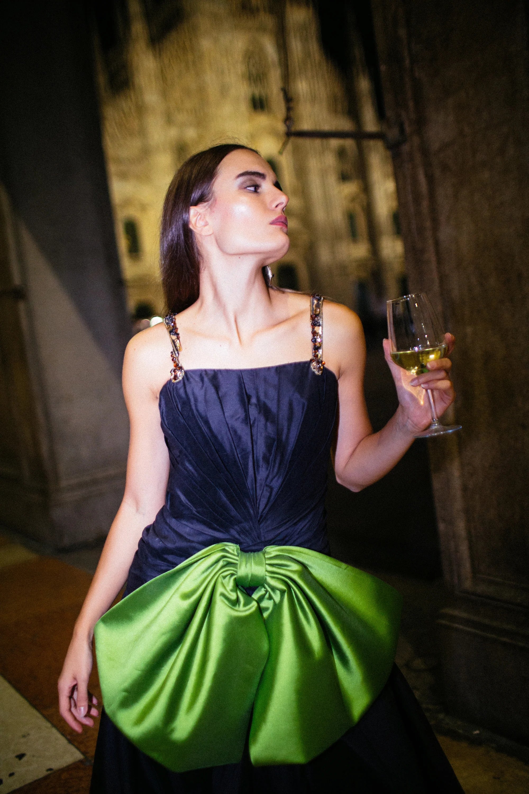 A navy gown with a large green satin bow gathered at the hip, photographed in Milan at night.