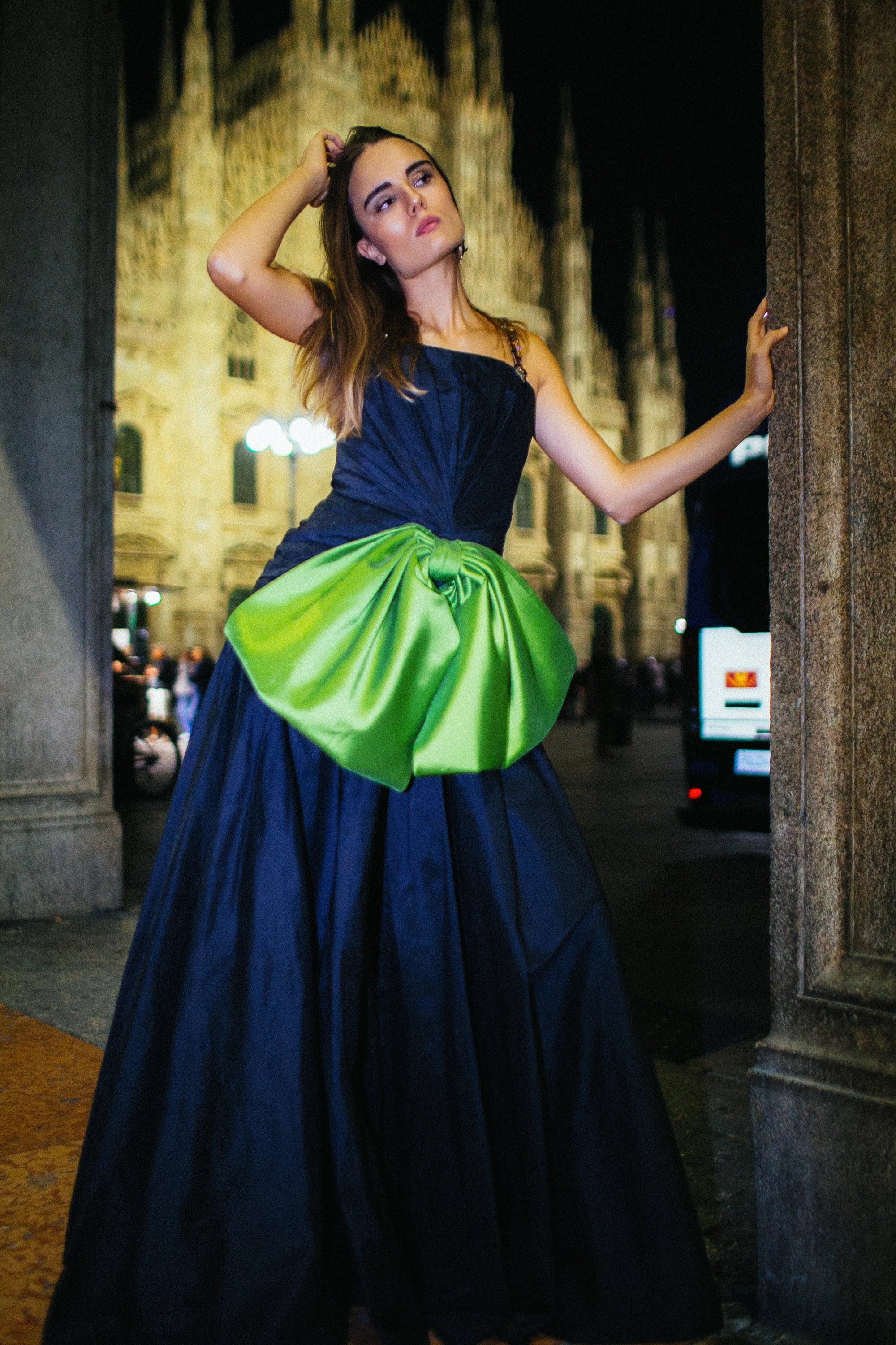 A navy gown with a large green satin bow gathered at the hip, photographed in Milan at night.