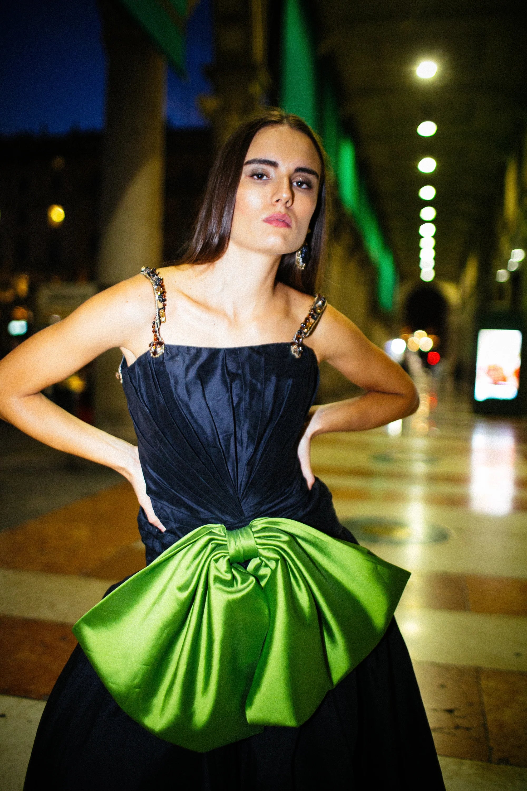A navy gown with a large green satin bow gathered at the hip, photographed in Milan at night.