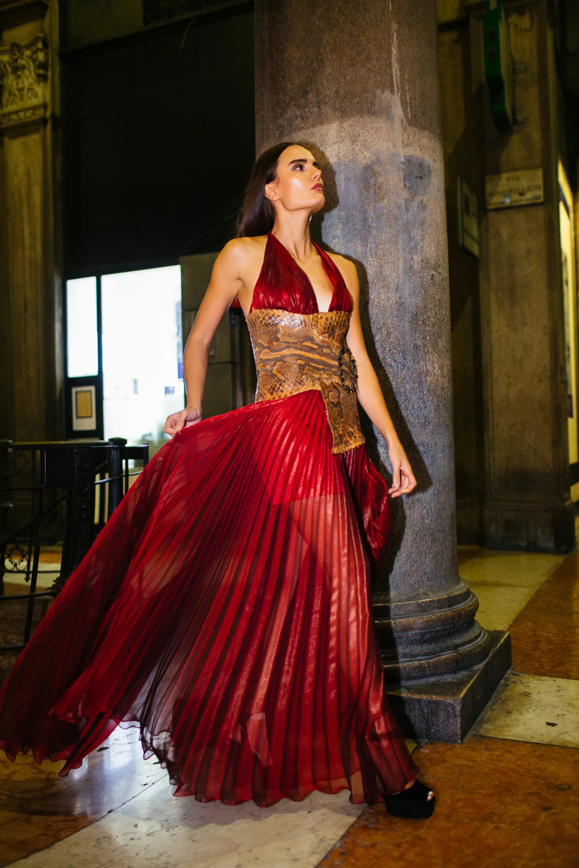 A red pleated gown with a gold worked bodice, photographed in the arcades of Milan at night.