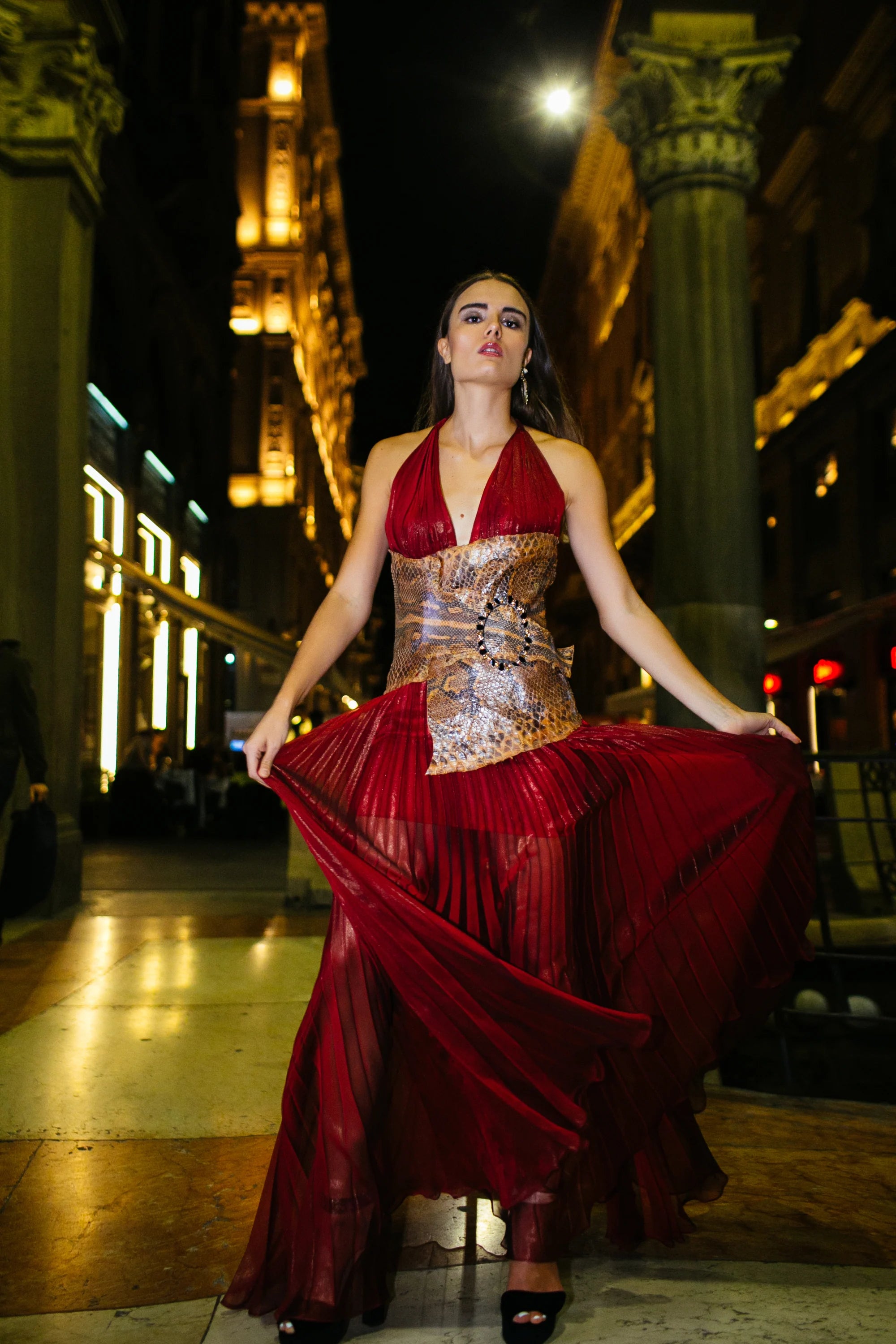 A red pleated gown with a gold worked bodice, photographed in the arcades of Milan at night.