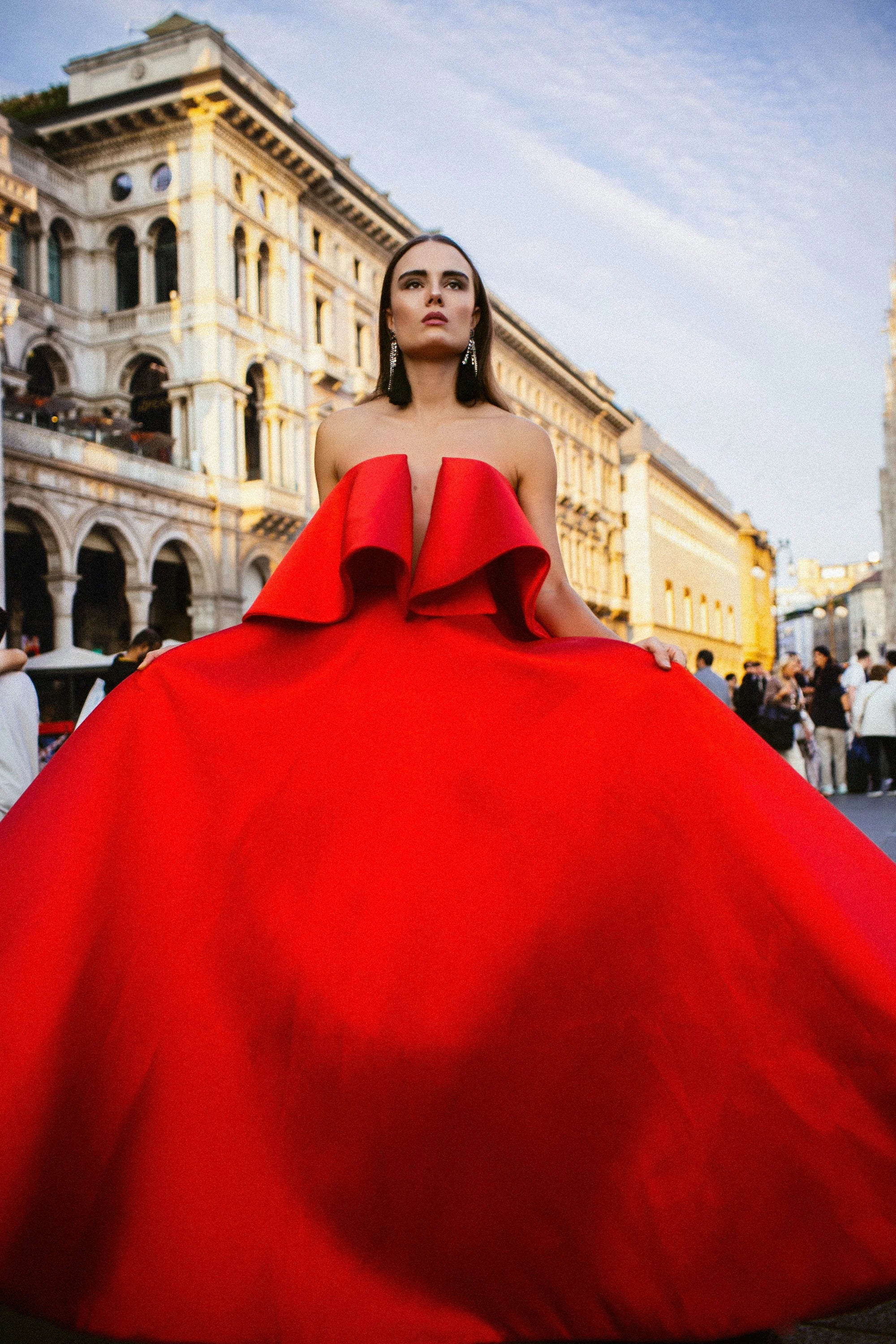 A red satin ballgown with a folded bow across the bust, photographed before the Duomo, Milan.