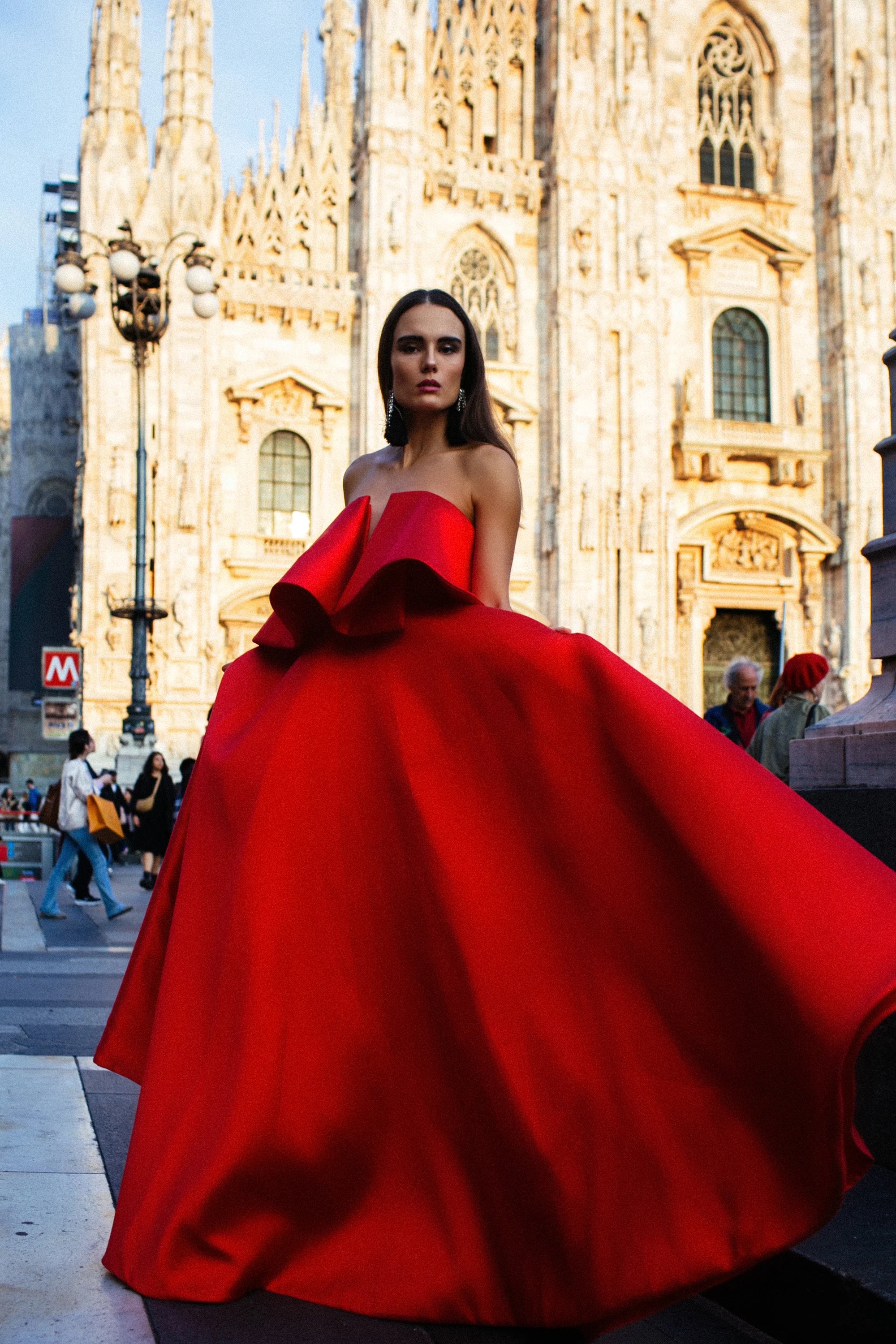 A red satin ballgown with a folded bow across the bust, photographed before the Duomo, Milan.